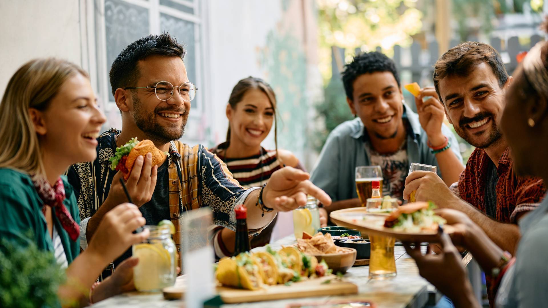 A group of restaurant patrons smiling and laughing as they enjoy plates of tacos at a Mexican restaurant.