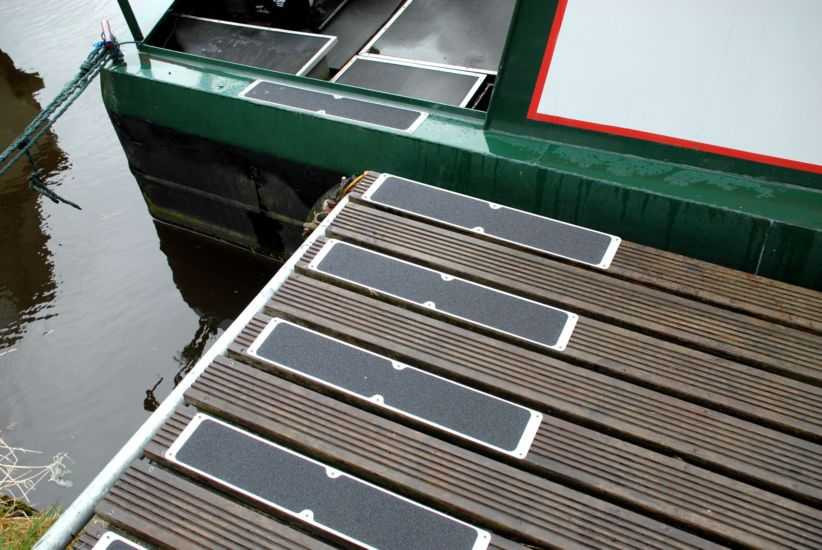 Heskins Bolt Down Anti-Slip Plates installed on a canal boat and dock deck — heavy-duty rectangular plates providing mechanically-fastened slip protection (shown with standard grit; photoluminescent glow surface available)