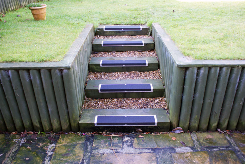 Heskins L-Shape Bolt Down Anti-Slip Plates installed on outdoor wooden garden steps — aluminum stair-nose plates with Safety-Grip coating for slip protection on wet or icy timber steps