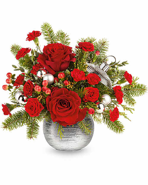Teleflora's Silver Sparkle Bouquet includes red roses, red spray roses, red miniature carnations, and red hypericum with cedar, Douglas fir, and parvifolia eucalyptus. Designed in Teleflora's Silver Sparkle Ornament, a ceramic ornament jar with silver metallic finish and ribbed texture. 
