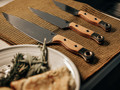 Benchmade 3 piece kitchen knife set showing a chef knife, utility knife, and paring knife on a table.