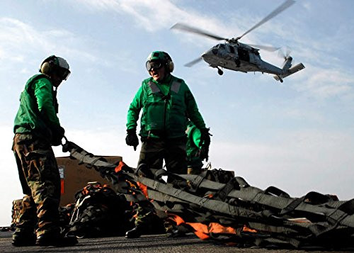 An MH-60S Seahawk passes over two Sailors as they pull a cargo net into position Poster Print by Stocktrek Images (17 x 11)