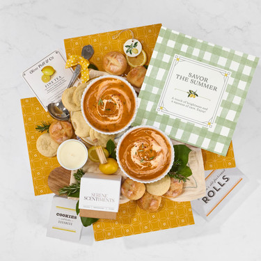 Overhead flat lay of comfort food gift items including soup, cookies, rolls, and insert cards arranged on a yellow patterned box.