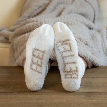 Pair of white fuzzy socks with "feel better" message in cream color on soles.