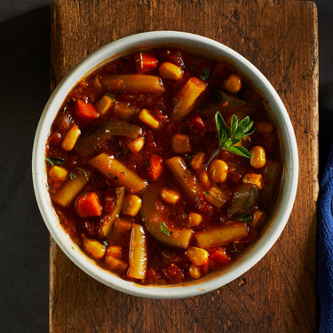 Close-up of a bowl of garden vegetable soup with carrots, corn, potatoes, green beans, and herbs in a tomato-based broth.