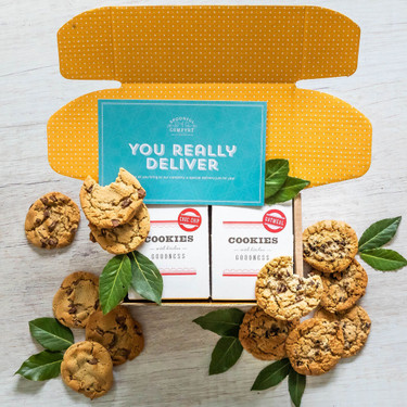 Open yellow gift box with assorted cookies and two boxes labeled “Cookies” with greenery and a blue card that reads “You Really Deliver.”