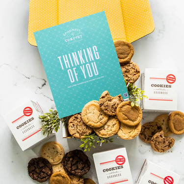 Open yellow gift box with assorted cookies, greenery, and a blue card that reads “Thinking of You.”