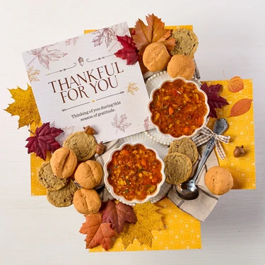 Soup package with a decorative insert, with two bowls of soup, rolls and cookies.