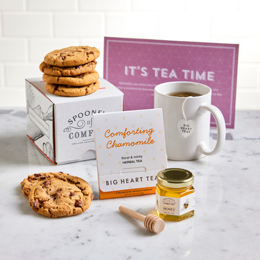 Tea-themed gift arrangement with cookies, a mug, chamomile tea, a jar of honey with a wooden dipper, and a card that reads “It’s Tea Time.”