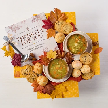 Soup package with a decorative insert, with two bowls of soup, rolls and cookies.