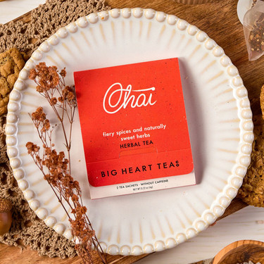 Autumn-themed tea display featuring a red Big Heart Tea Co. tea package on a decorative white plate, surrounded by cookies, acorns, dried flowers, and a cup of tea.