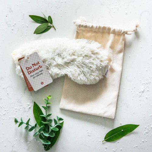 White faux-fur eye mask display atop a canvas drawstring bag