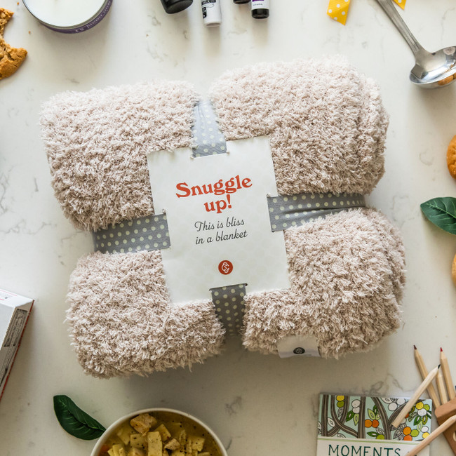 Cozy Blanket wrapped in a gray polkadot ribbon with a label with text that reads "Snuggle Up! This is bliss in a blanket."