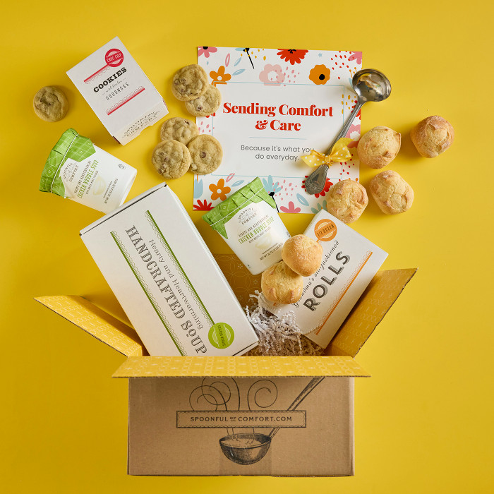 Open Spoonful of Comfort gift box with rolls, cookies, two containers of soup, a box labeled “Handcrafted Soup,” and a floral card that reads “Sending Comfort & Care,” with additional rolls and cookies arranged around the box.