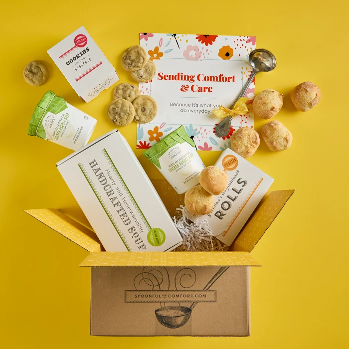 Open Spoonful of Comfort gift box with rolls, cookies, two containers of soup, a box labeled “Handcrafted Soup,” and a floral card that reads “Sending Comfort & Care,” with additional rolls and cookies arranged around the box.