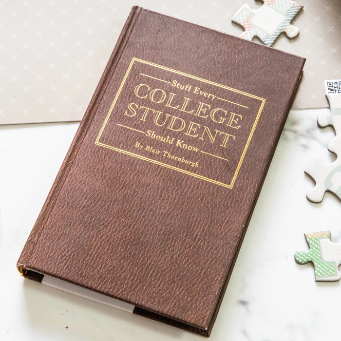 Close-up of a brown book titled “Stuff Every College Student Should Know” placed on a surface with scattered puzzle pieces nearby.