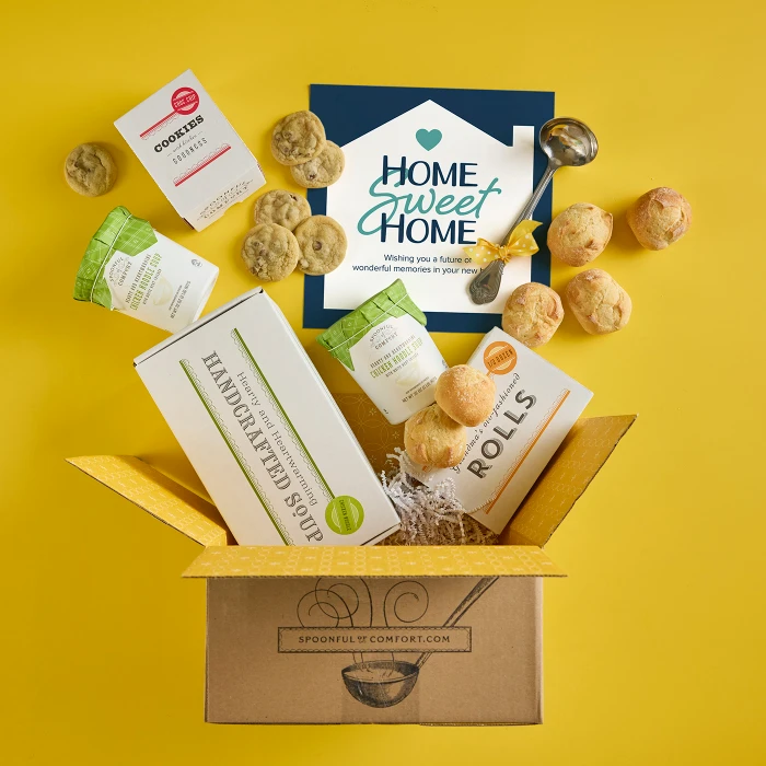 Open Spoonful of Comfort gift box with rolls, cookies, a container labeled “Handcrafted Soup,” and a card that reads “Home Sweet Home,” with rolls and cookies arranged around the box on a yellow background.