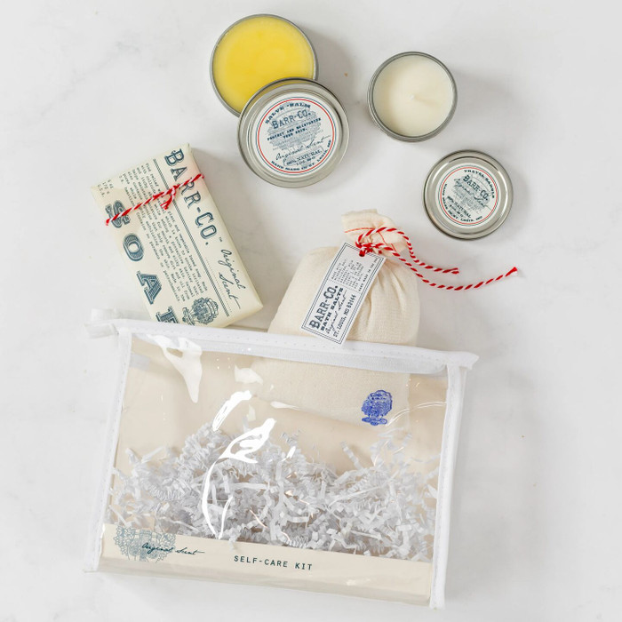 Overhead view of a yellow gift box arrangement with two bowls of soup, rolls, cookies, a container labeled “Handcrafted Soup,” a robe, self-care items in a toiletry bag, and a card that reads “Time to Relax.”