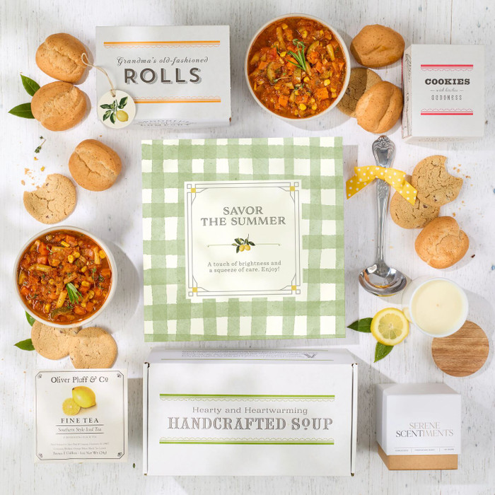 Styled display of soup, baked goods, and “Savor the Summer” packaging arranged on a light tabletop with yellow accents.