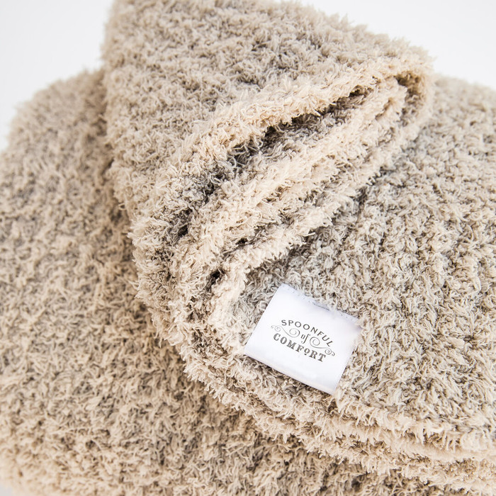 Close up image of folded plush creme throw blanket with Spoonful of Comfort tag