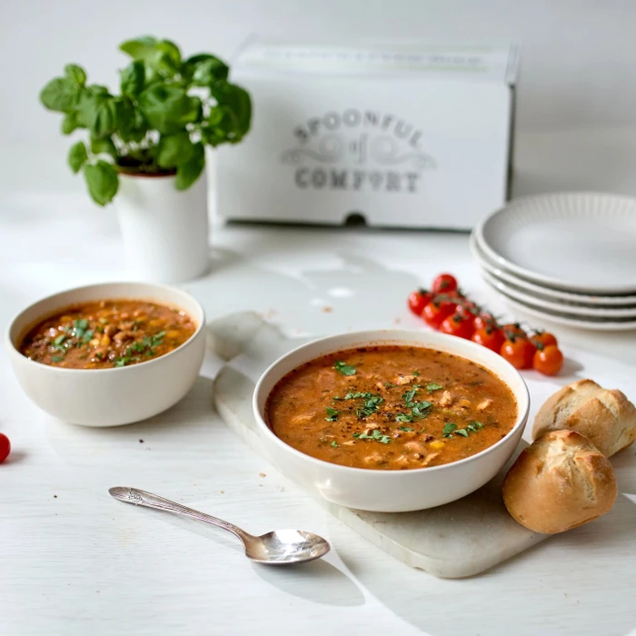 Two bowls of soup on a table with bread rolls and a spoon beside them.