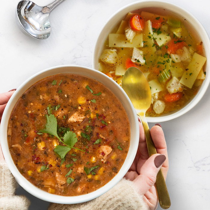 Two bowls of soup- one chicken noodle and the other chicken tortilla flavors, the chicken tortilla being held with a spoon in hand.