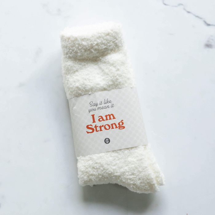 Pair of fuzzy white socks with "Say it like you mean it I am Strong" message in in black and red