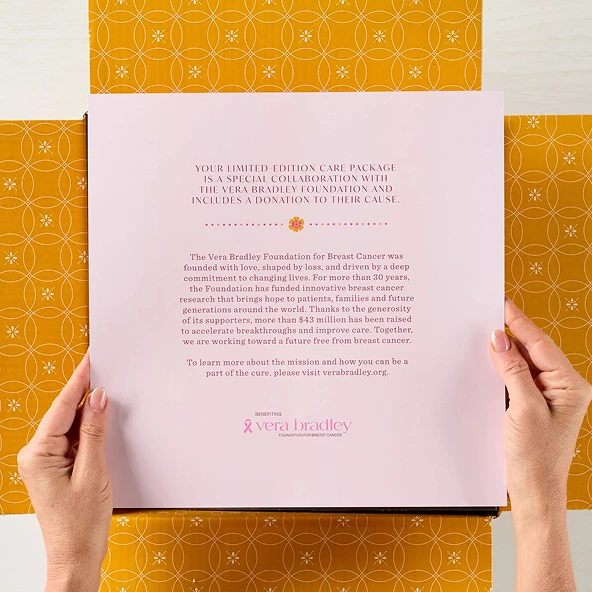 Hands holding open a gift box displaying a printed message, with yellow patterned packaging surrounding the box.