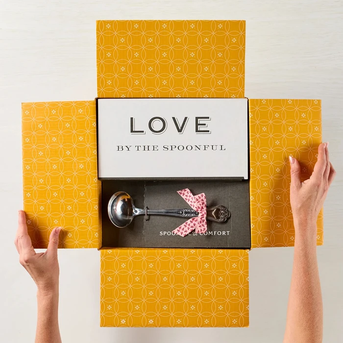 Open faced box with the insert "Love by the Spoonful" being held by two hands, with a curated "Vera Bradley" Print bow
