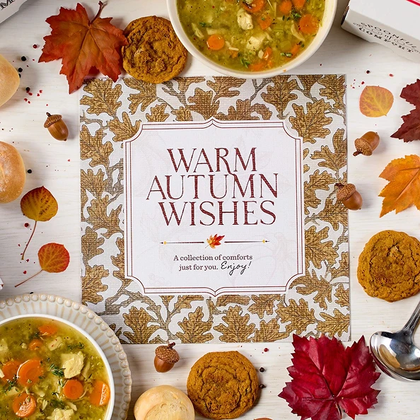 Overhead image displaying "Warm Autumn Wishes" card, Spoonful of Comfort Box, styled with soups, rolls and cookies.