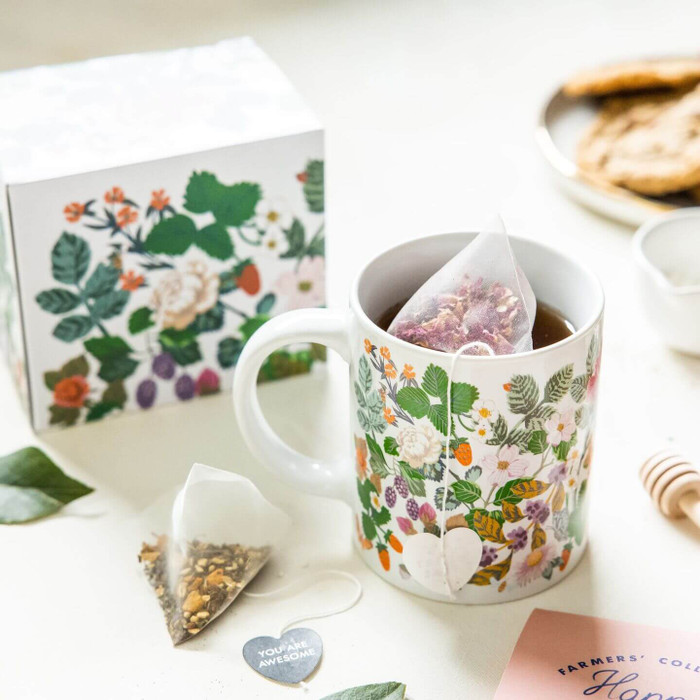A lifestyle table top image of Helmsie-designed Berry Blooms print mug filled with Happy Rooibos Tea