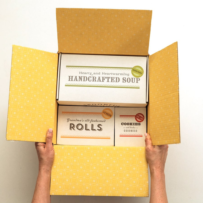 A Spoonful of Comfort shipping box opened to display a yellow printed interior and the product boxes nestled inside.