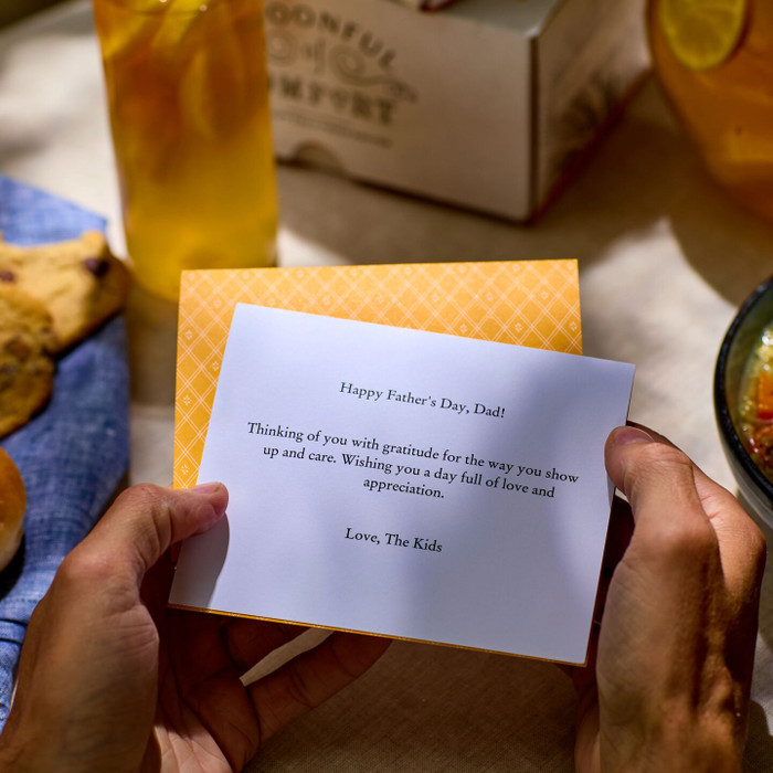 Close-up of hands holding a card that reads “Happy Father’s Day, Dad! Thinking of you and grateful for all you do. Love, The Kids,” with soup, cookies, and a drink in the background.