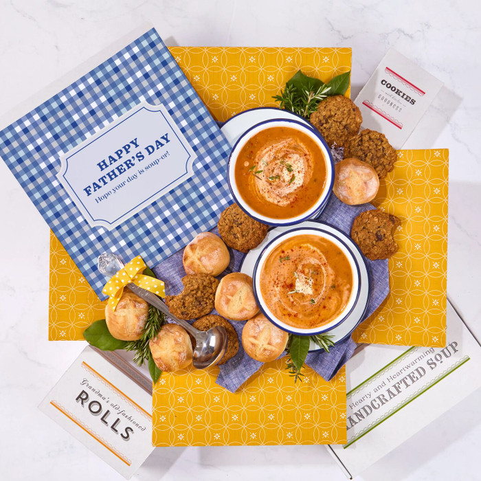 Overhead view of a Father’s Day gift arrangement with two bowls of soup, rolls, cookies, a container labeled “Handcrafted Soup,” a metal ladle with a yellow ribbon, and a blue checkered card that reads “Happy Father’s Day.”