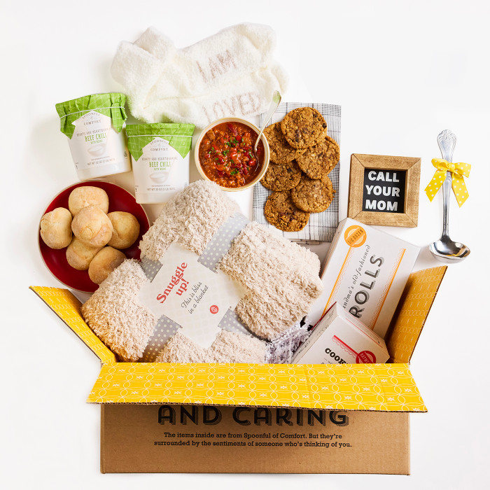 Open Spoonful of Comfort gift box filled with a bowl of soup, rolls, cookies, two containers of soup, a cozy knit throw blanket, a metal ladle with a yellow ribbon, and a framed picture that reads “Call Your Mom.”