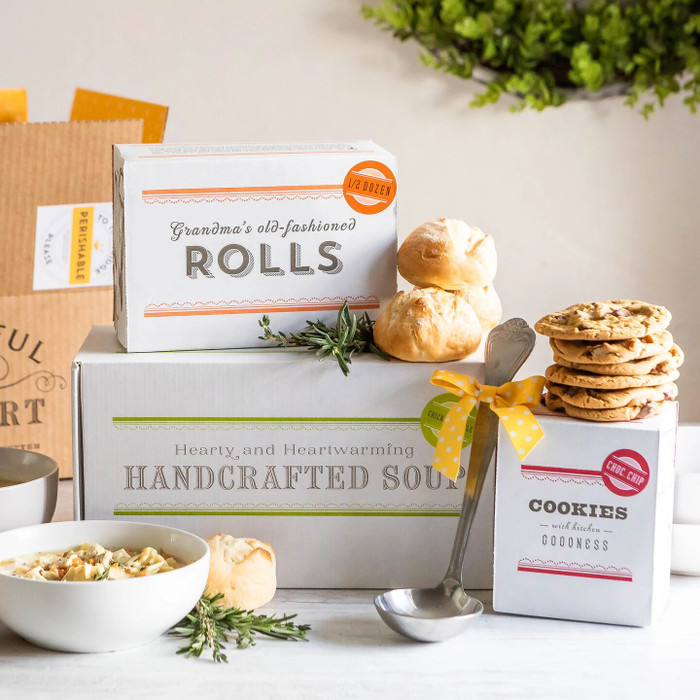 Soup gift set displayed with a bowl of soup, rolls, cookies, boxes labeled “Chicken Soup,” “Rolls,” and “Cookies,” and a metal ladle with a yellow ribbon.