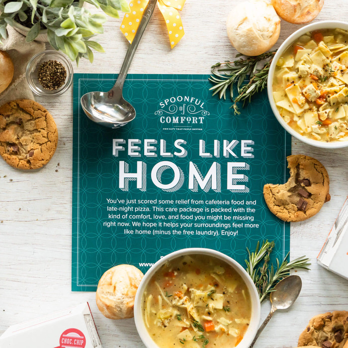College Care Package insert with text "Feels Like Home" displayed on top of a table with two bowls of soup, chocolate chip cookies, rolls and a ladle.
