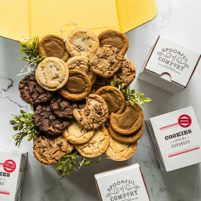 Overhead view of assorted cookies arranged on a surface with several Spoonful of Comfort cookie boxes and small sprigs of greenery.