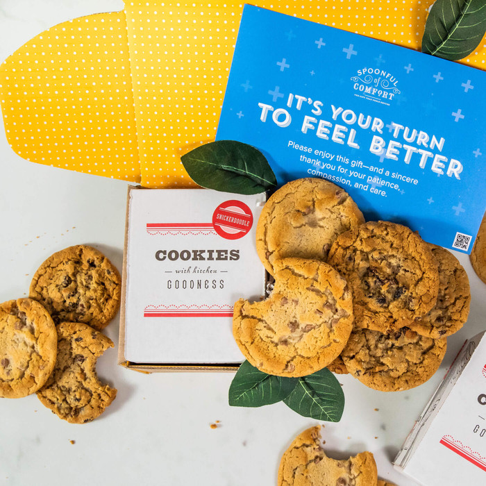 Open yellow gift box with assorted cookies, boxes labeled “Cookies Goodness,” greenery, and a blue card that reads “It’s Your Turn to Feel Better.”