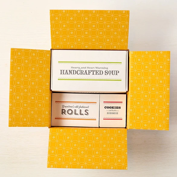 Open box displaying three containers, soup, rolls and cookies
