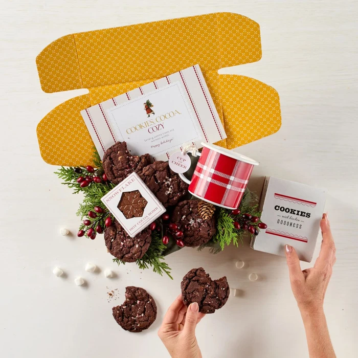 Festive Holiday Cookie Package with a decorative insert, and surrounded by cookie boxes and mugs.