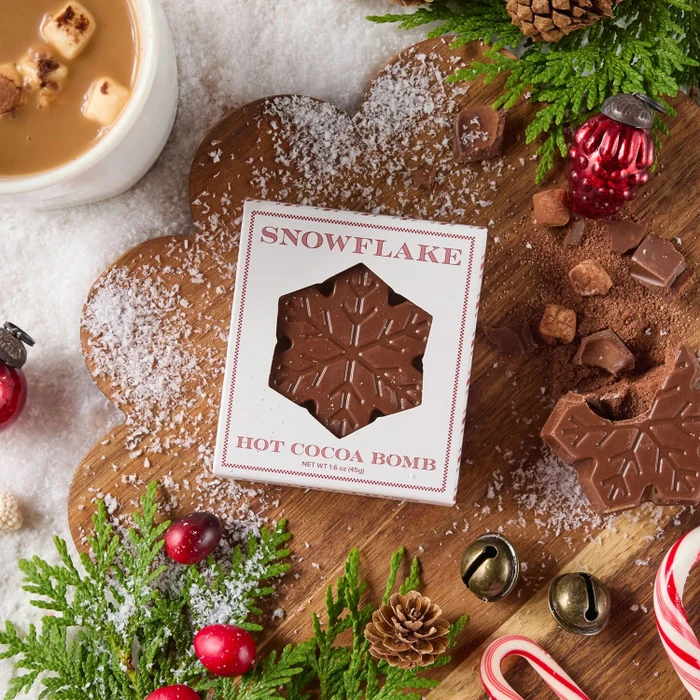 Snowflake Hot Cocoa Bomb with a wooden background with fresh snow beside it.