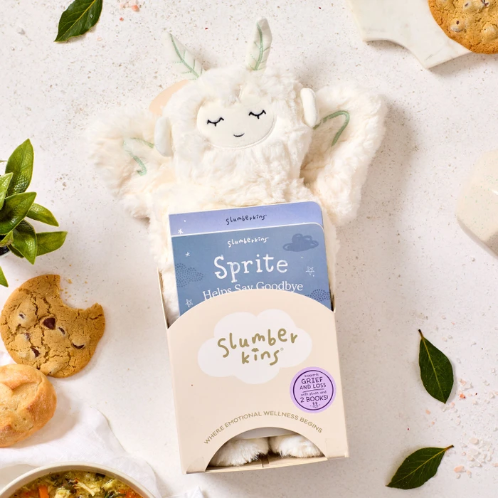 Close-up of a plush Sprite toy packaged in a “Slumberkins” box labeled “Sprite,” surrounded by cookies, greenery, and a bowl of soup partially visible nearby.