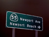Photorealistic oil painting of an illuminated Newport Avenue and Newport Beach road sign glowing against a dark night sky.