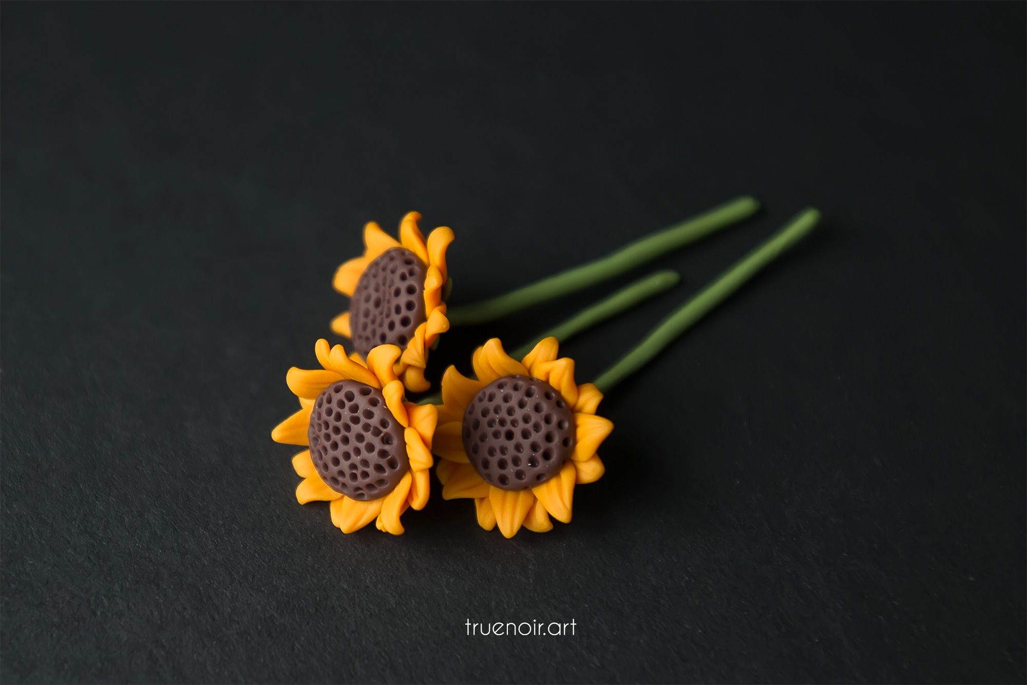 Three polymer clay figurines of miniature sunflowers against a black background