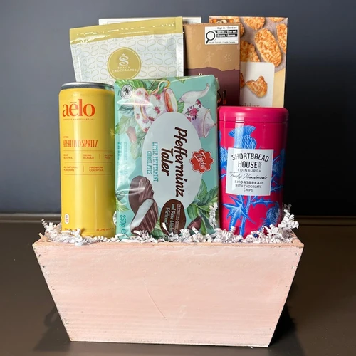 A beautiful pastel wooden container over flowing with treats for mom! She will enjoy the Shortbread House chocolate chip shortbread cookies as well as the savoury crackers, Heidi chocolate bar and the Aelo Aperativo Spritz drink mix!  