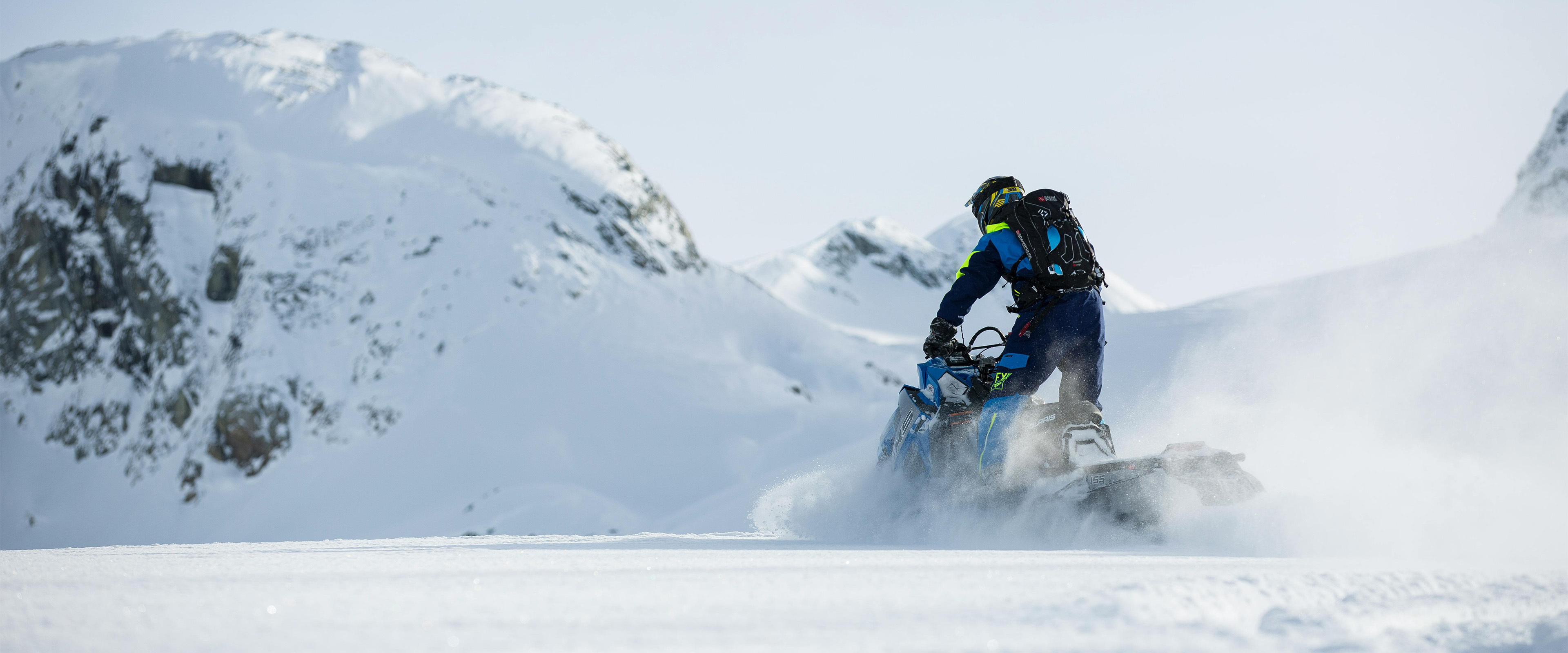 Snowmobiler on a snowy mountain ridge, assessing the signs of avalanche danger in backcountry terrain.