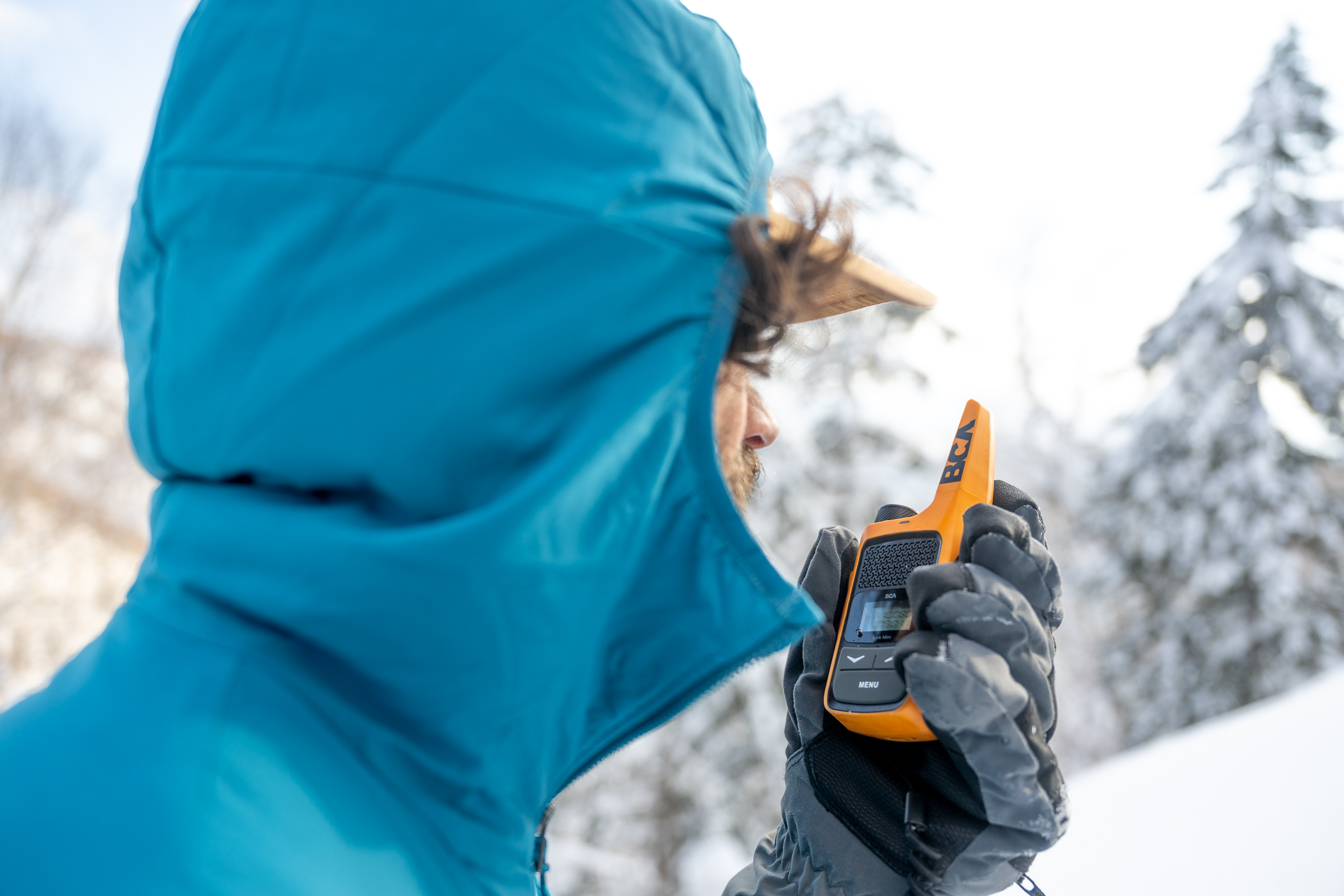 Nick Russell in a blue jacket using an orange BCA radio in a snowy forest