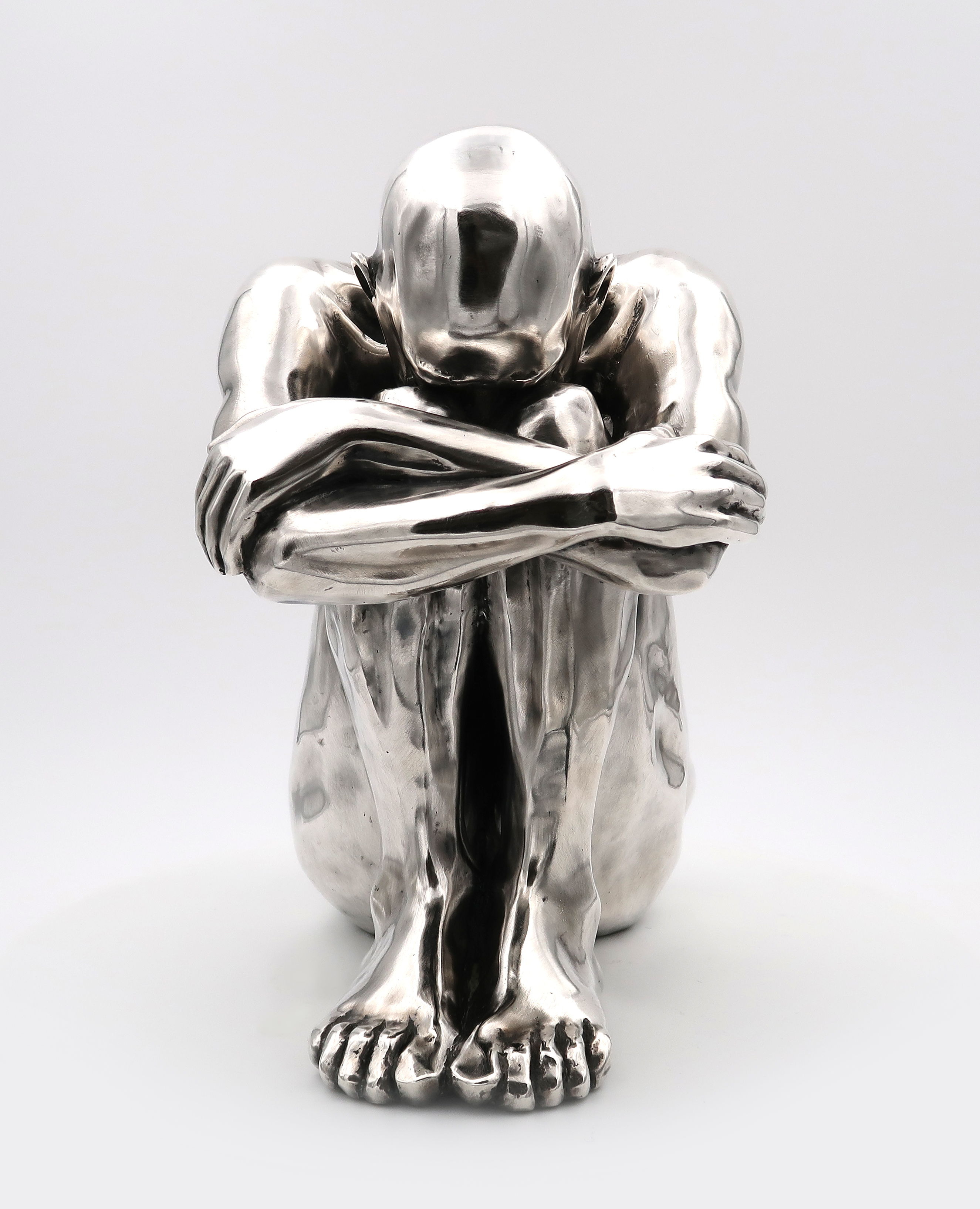 Photo de la sculpture contemporaine en métal argenté représentant un homme en position fœtus proposé par la galerie en ligne Design by Jaler