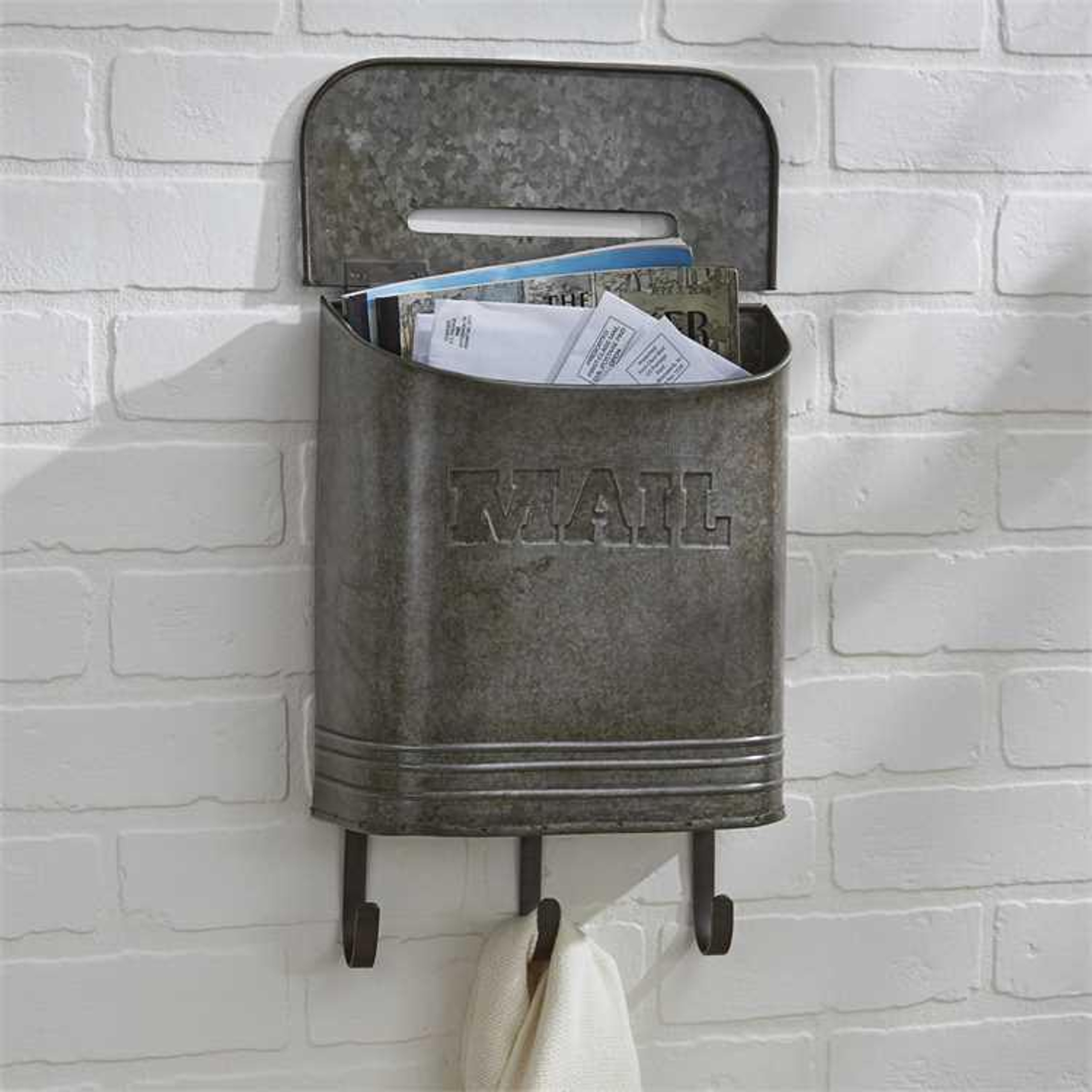 Galvanized mailbox with hooks on a white brick wall